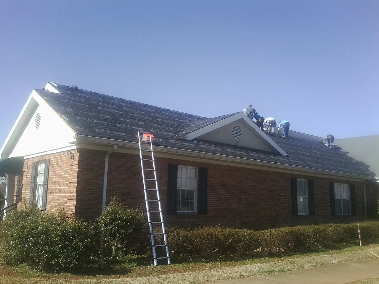 Crew tearing shingles off a brick ranch roof with a ladder set — Emergency Roof Repair work by our crew in Morton