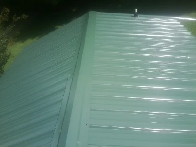 New green metal panels meeting at the ridge of a roof — Flat Roof Repair work by our crew in Morton