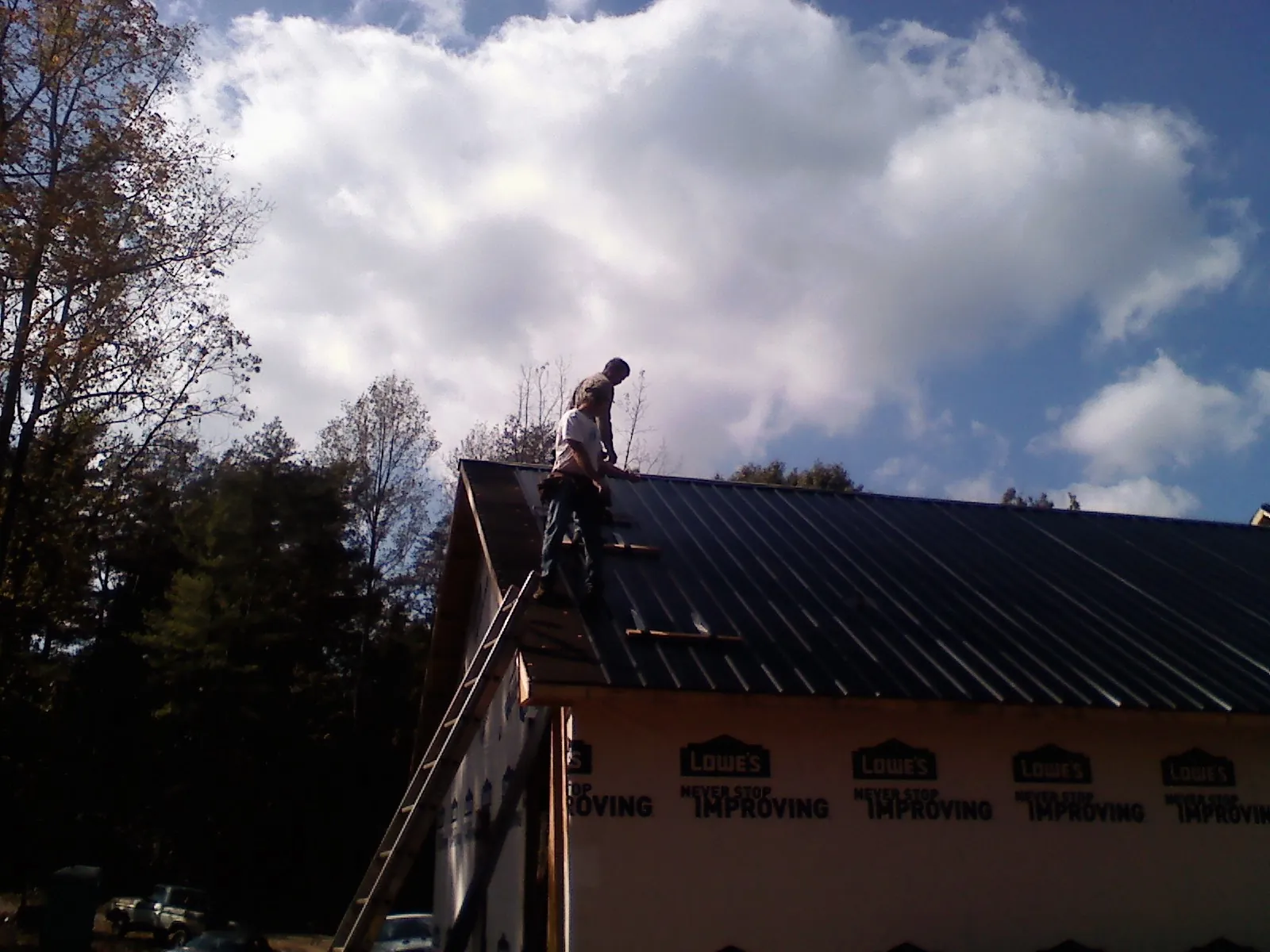 Roofer fastening dark metal panels high against a cloudy sky, from a Roof Inspection job in Morton